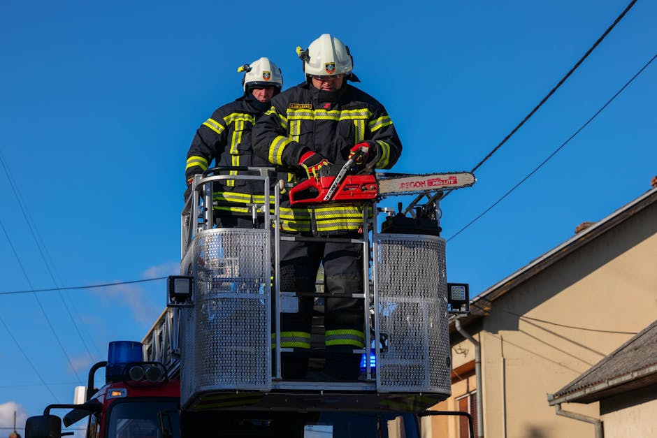 Firefighters in action on a ladder truck, using a chainsaw for rescue operations under a clear blue sky.