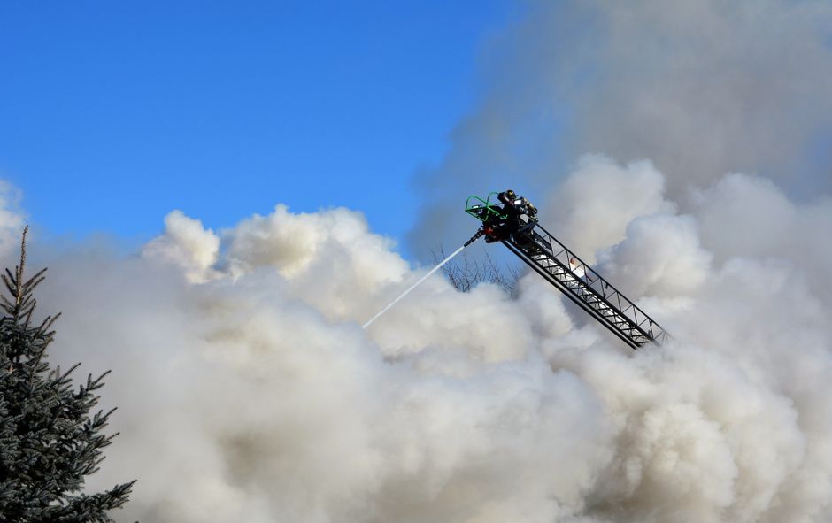 Firefighters extinguishing fire using an aerial ladder amidst heavy smoke with blue sky backdrop.